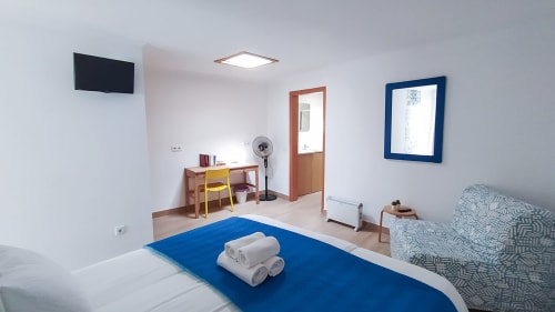 Quarto espaçoso em Ó da Casa em Peniche com cama de destaque azul, secretária, TV e vista para o jardim