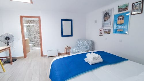 Quarto azul e branco na Ó da Casa BnB em Peniche com porta de madeira, ventilador e arte de parede temática de bonde