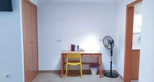 Quarto moderno na pousada Ó da Casa em Peniche com escrivaninha de madeira, cadeira amarela, ventilador de pé e paredes brancas
