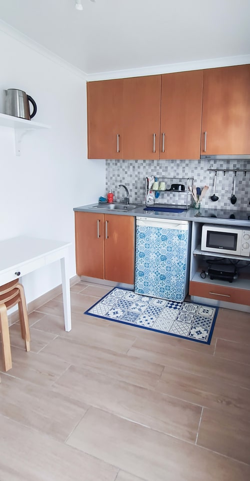 Pequena cozinha com armários terracota, painel traseiro com padrão azul, micro-ondas e pia na pousada Ó da Casa