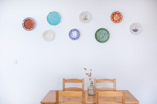 Salle à manger de la maison d'hôtes Ó da Casa à Peniche avec table en bois, chaises et assiettes décoratives sur mur blanc