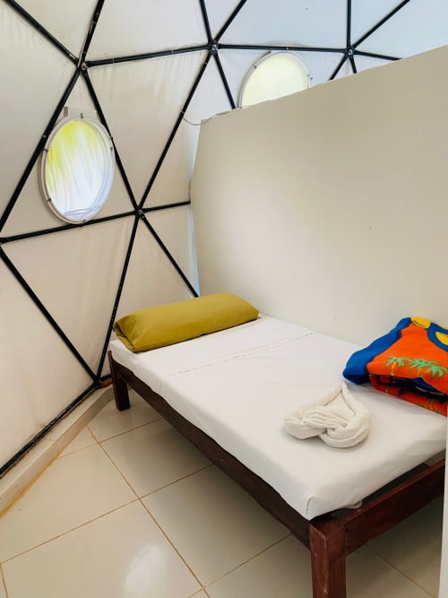 Acogedora habitación en el hostal Cayuco Maya de Bacalar con cama, almohada amarilla y techo estilo tienda geométrico