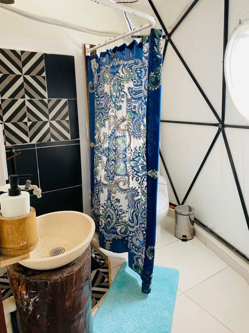 Baño ecléctico en el hostal Cayuco Maya de Bacalar con lavamanos de cerámica, cortina de ducha azul estampada y azulejos geométricos