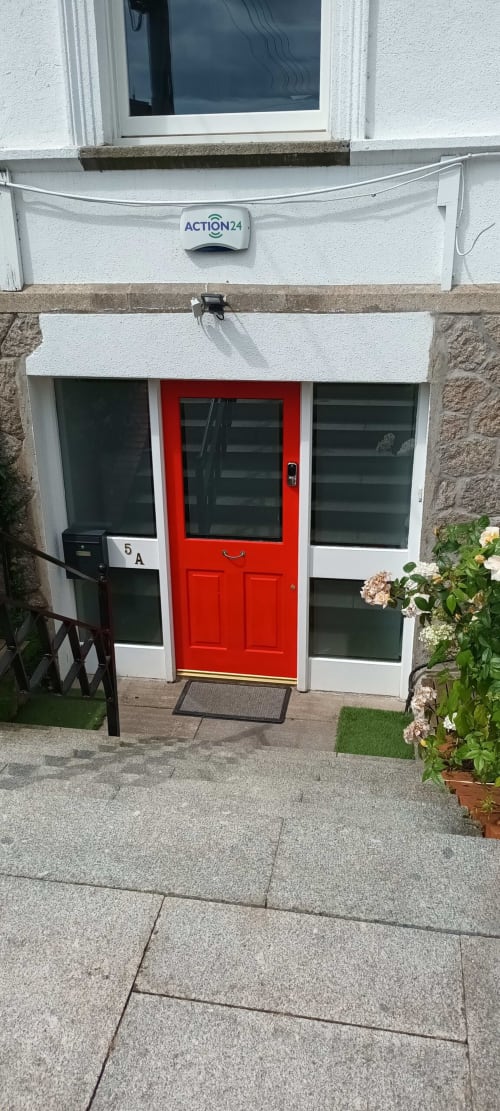 Red door entrance to Eglinton Road Bray guesthouse with white facade, windows, and flowering plants