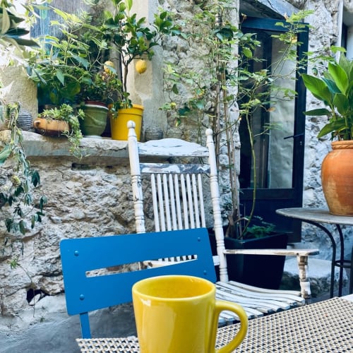 Charmante cour de La vie de château B&B à Grignan avec chaise bleue, tasse jaune et plantes en pot contre les murs en pierre