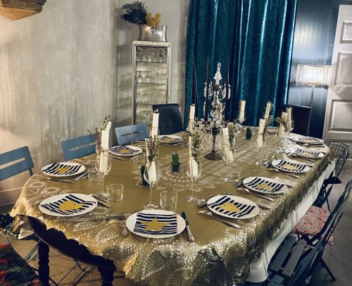 Élégante salle à manger à La vie de château avec nappe à paillettes dorées, chargeurs rayés et rideaux en velours bleu canard à Grignan.