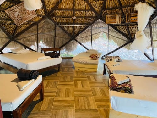 Amplia habitación compartida en el hostal Cayuco Maya de Bacalar con múltiples camas, piso de madera y techo de palapa