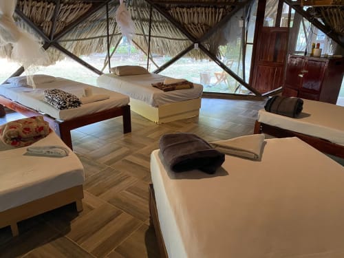 Múltiples camas con sábanas blancas y toallas oscuras en una spaciosa habitación de hostal en Cayuco Maya, Bacalar, con techo de paja y