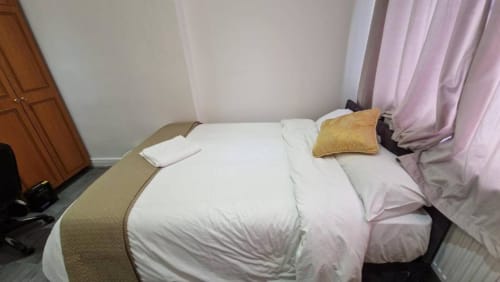 Modern hotel bedroom at Starlet Property London with white bedding, gold cushion, and pink curtains
