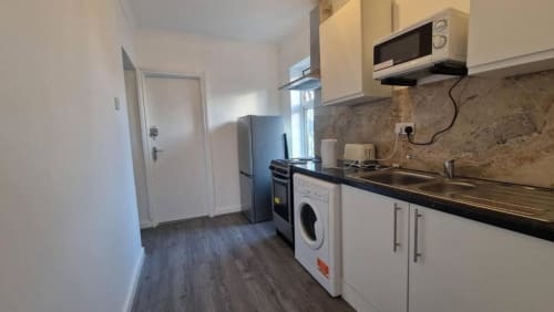 Modern kitchen in Starlet Property London hotel room with white cabinets, black countertop, stainless steel appliances,