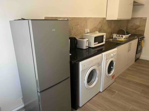 Modern kitchen at Starlet Property London with stainless steel refrigerator, black countertop, white washing machines,