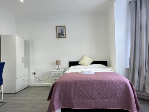 Modern bedroom at Starlet Property London with purple quilted bedcover, white wardrobes, and pine tree artwork