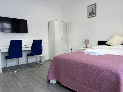Modern hotel room at Starlet Property London with purple bedding, navy chairs, desk, wardrobe, and wall-mounted TV