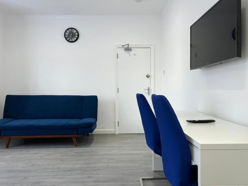 Modern hotel room at Starlet Property London with blue sofa bed, desk with blue chairs, wall-mounted TV, and white walls