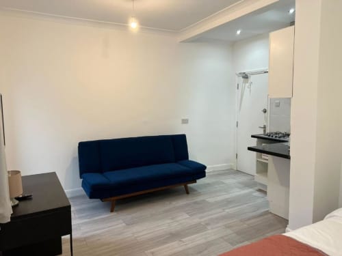 Modern studio room at Starlet Property London with blue sofa bed, kitchenette, and wood flooring
