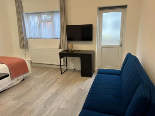 Modern hotel room at Starlet Property London with blue sofa, black desk, TV, and hardwood flooring