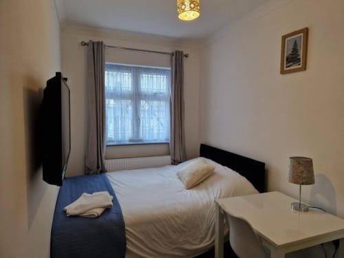 Bright, compact bedroom at Starlet Property London with white bedding, black headboard, large window with gray curtains, and