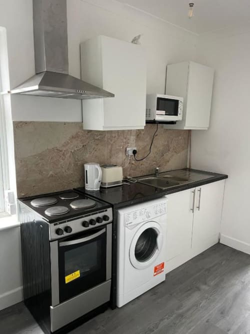 Modern kitchenette at Starlet Property London with stove, washing machine, microwave, and white cabinetry