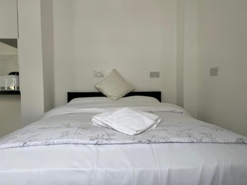 Clean studio bedroom at Starlet Property London with black bed frame, white linens, cream pillow, and folded towel