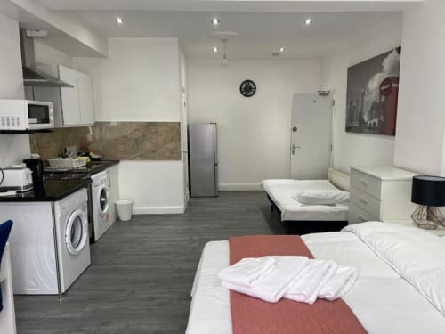 Studio apartment at Starlet Property London featuring twin beds with red runners, kitchenette, and washing machines