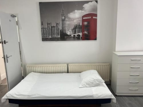 Modern London studio bedroom with white bedding, radiator heating, dresser, and Big Ben artwork above bed at Starlet Property