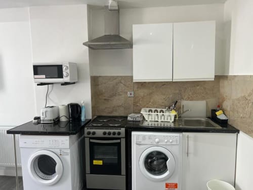 Modern kitchen in London apartment with washing machines, electric stove, white cabinets, and black countertops at Starlet