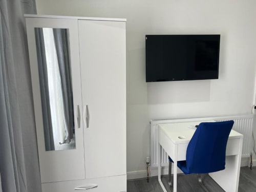 Studio 1 bedroom with white wardrobe, desk, blue chair, wall-mounted TV, and radiator at Starlet Property London