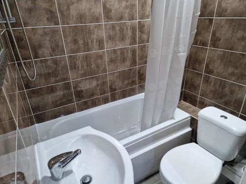 Modern bathroom in Starlet Property studio apartment, London, with brown tile walls, white sink, toilet, bathtub and shower