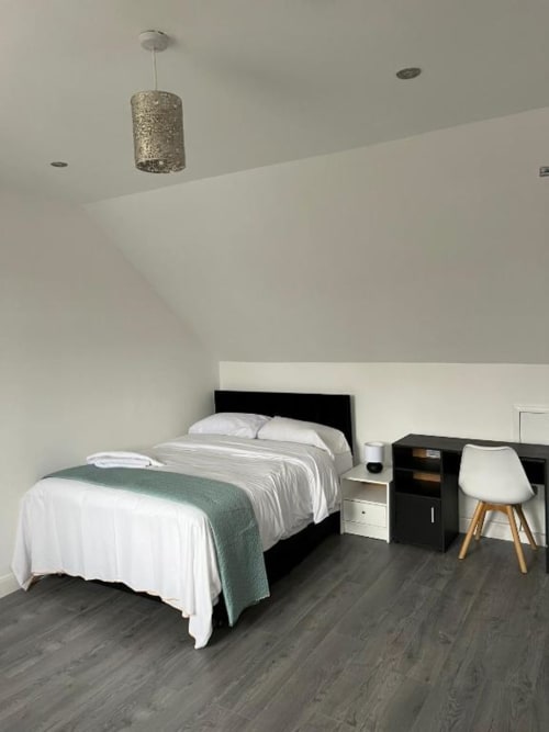 Modern loft studio bedroom at Starlet Property London with black bed, white linens, desk, chair, and pendant light above dark