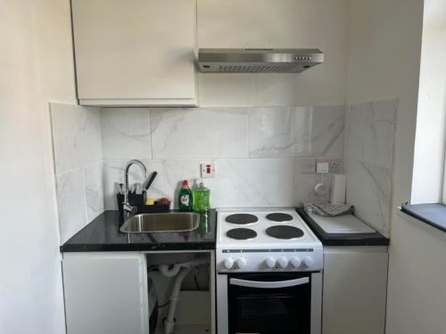Compact kitchenette in Starlet Property London loft studio with stove, oven, sink, and black countertop