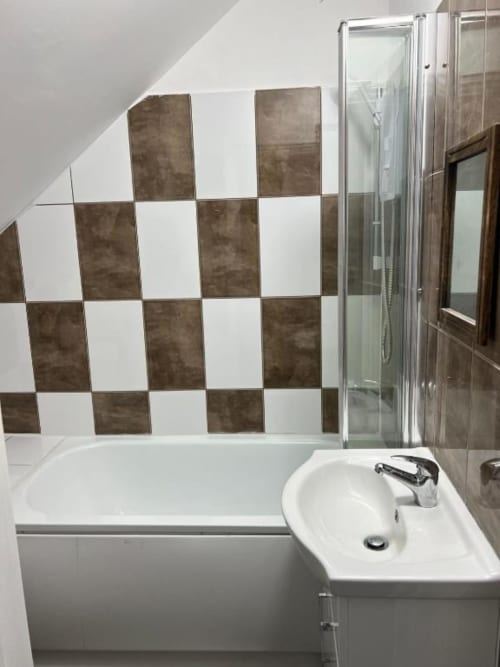 Modern bathroom in Starlet Property Loft Studio with brown and white checkered tile wall, white bathtub, sink, and glass