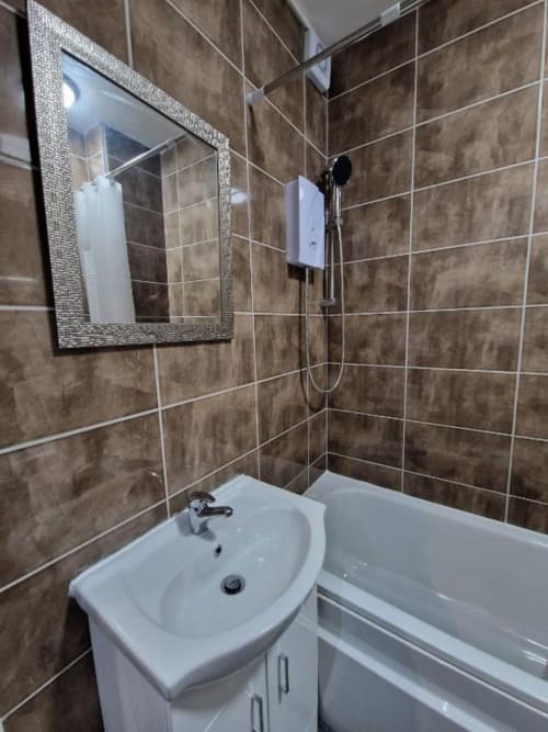 Modern bathroom at Starlet Property London with brown tiled walls, white sink vanity, bathtub, mirror, and shower fixtures