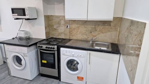 Studio kitchen at Starlet Property London with washing machine, oven, stove, microwave, and sink against tiled backsplash