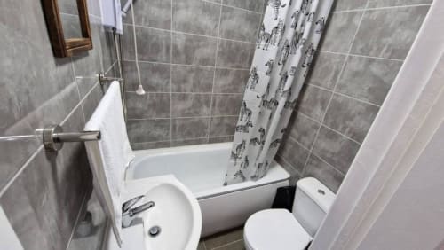 En-suite bathroom at Starlet Property London with white bathtub, toilet, gray tiles, and animal-print shower curtain.