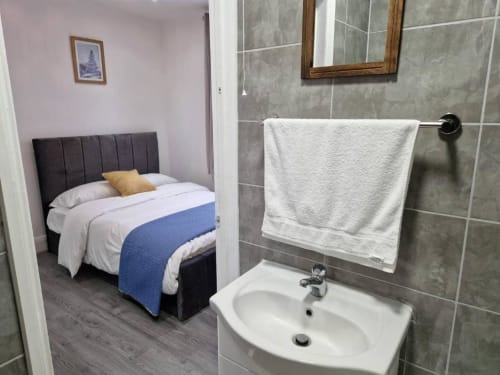 En-suite bedroom at Starlet Property London with queen bed, grey tiled bathroom, white sink, and towel rack