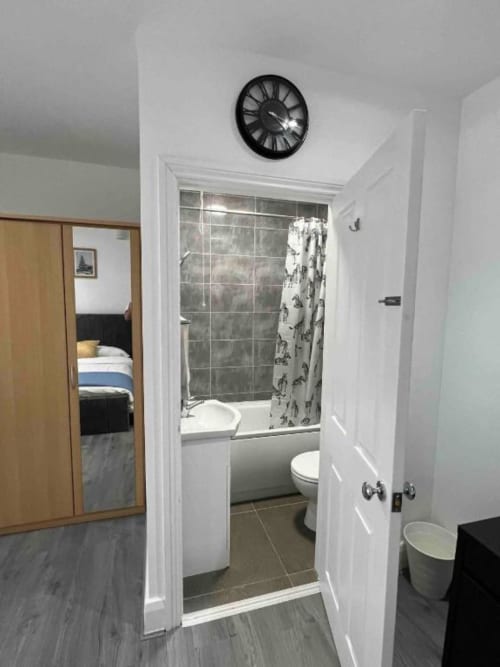 Starlet Property London en-suite bathroom with white walls, gray tile shower, toilet, and clock above doorway entrance