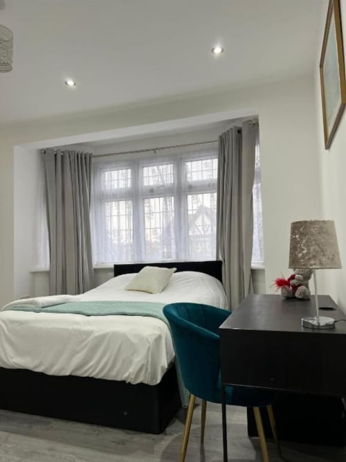 Modern bedroom at Starlet Property London with black bed, white linens, teal chair, gray curtains, and windows