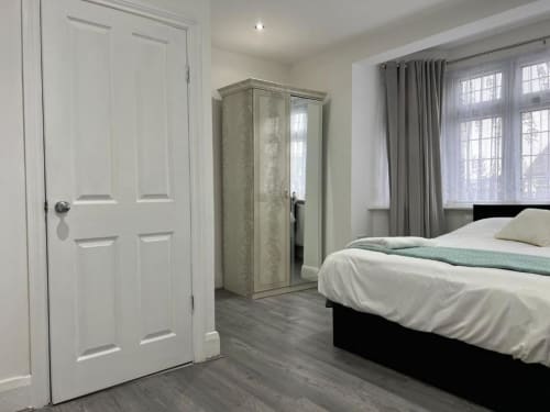 Modern bedroom at Starlet Property, London with black bed, white wardrobe, mirrored armoire, and grey curtains