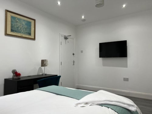 Modern bedroom at Starlet Property London with wall-mounted TV, black desk, white bedding, and ensuite bathroom door.