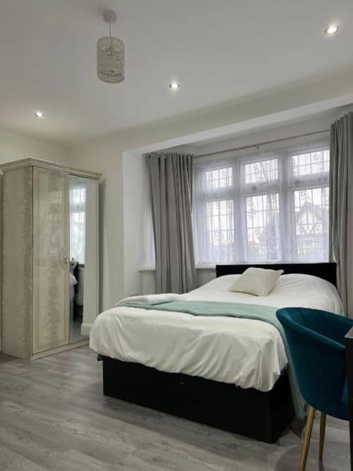 Modern en-suite bedroom at Starlet Property London with black bed, white linens, large windows, grey curtains, and