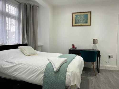 Modern bedroom at Starlet Property London with white bed, turquoise accents, desk, and large window with curtains