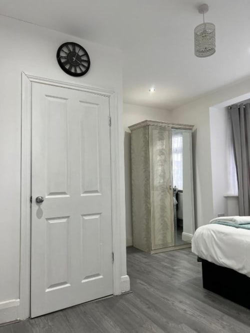 Modern bedroom at Starlet Property London with white door, mirrored wardrobe, bed, clock, and pendant light fixture