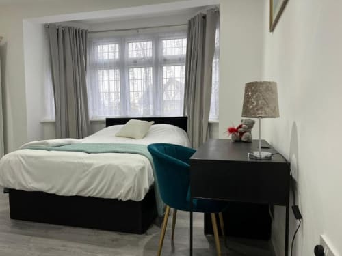 Modern bedroom at Starlet Property London with black bed, teal chair, desk, and large windows with grey curtains