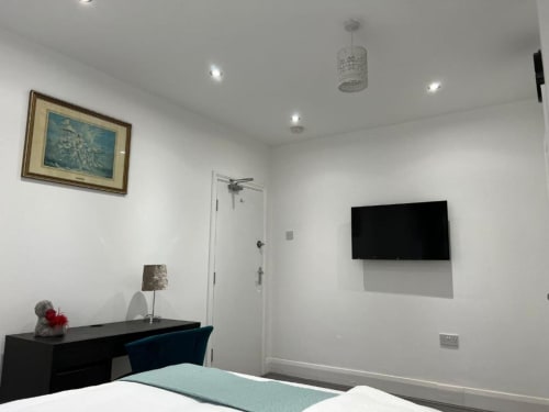 Modern en-suite bedroom at Starlet Property London with wall-mounted TV, desk with lamp, and en-suite bathroom door