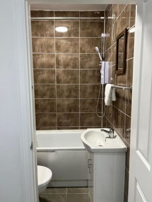 Modern bathroom at Starlet Property, London with brown tiled shower, white sink, toilet, and walk-in shower enclosure