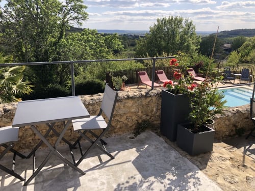 Terrasse ensoleillée du Château Haut Clarise avec table à manger, transats roses, vue sur la piscine et paysage campagnard