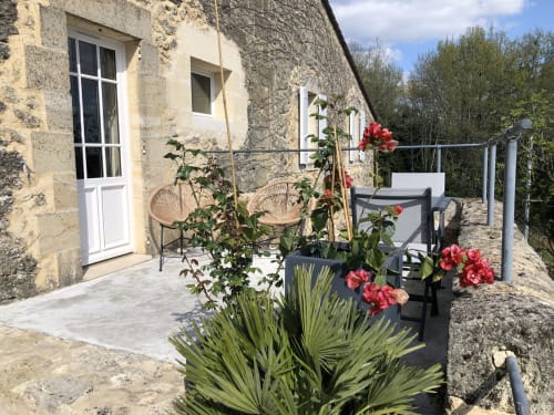 Terrasse en pierre du Château Haut Clarise avec fleurs rouges, fauteuils en osier et vue sur la campagne à Belvès-de-Castillon