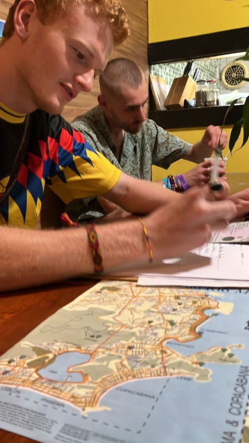 Hóspedes planejando viagem no Hostel New Ipanema com mapa do Rio de Janeiro, discutindo itinerário