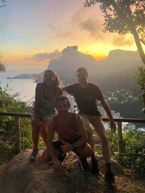 Três hóspedes apreciam o pôr do sol com vista das montanhas e litoral do Rio no mirante do Hostel New Ipanema