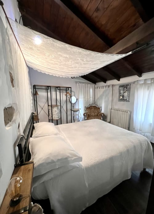 Chambre lumineuse avec lit à baldaquin blanc, poutres apparentes et vue sur le jardin à l'Agritusmo Stecadò à Dolceacqua